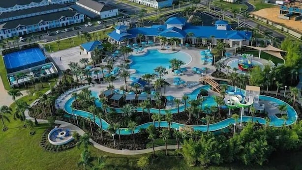 Vista aérea de un resort con varias piscinas, palmeras y un tobogán de agua.
