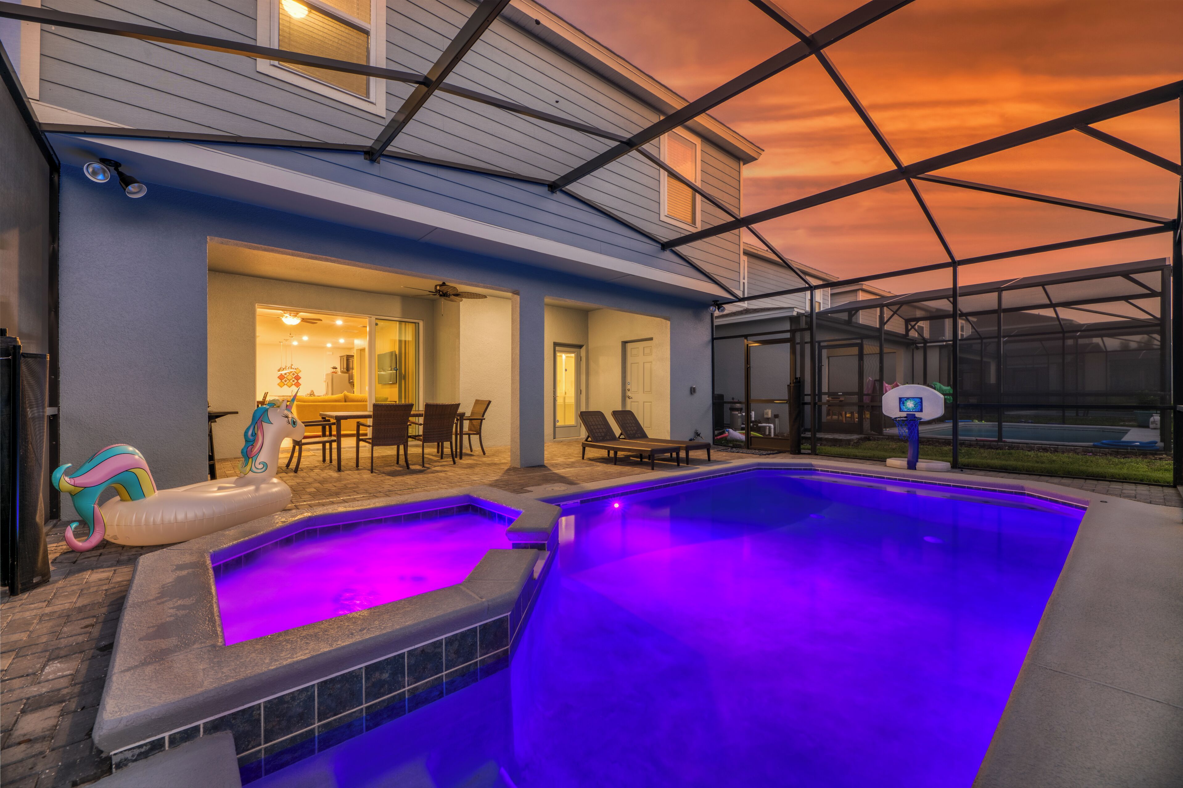 An outdoor swimming pool with a hot tub, lounge chairs, and a basketball hoop.