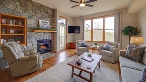 A living room with a stone fireplace, a ceiling fan, and a large window. - Hike & Ski: Mtn-View Gem w/ Balcony in Burnsville! (Burnsville)