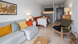 A living room with a sofa, a dining table with chairs, a lamp, and a painting on the wall.