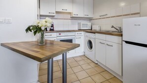 Eine moderne Küche mit weißen Schränken, einem Holztisch, einer Waschmaschine, einer Mikrowelle und einem Kühlschrank.