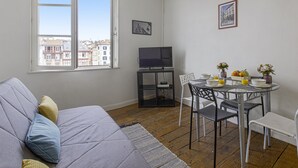 Ein kompakter Wohnraum mit Sofa, Esstisch und Stühlen, Fernseher und einem Fenster mit Blick auf die Stadt.