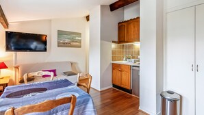 Un espacio habitable compacto con kitchenette, una zona de comedor con mesa y sillas, un televisor montado en la pared y un cubo de basura.