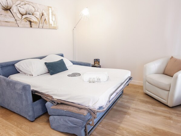 A bedroom with a bed, a chair, a bedside table, and a lamp. - Studio Faidherbe - Welkeys (Les Lilas)