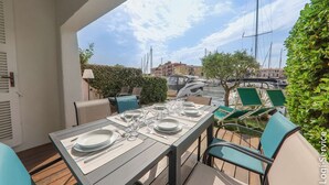 Un espace de restauration en plein air avec une table dressée pour quatre personnes, des chaises et une vue sur le port de plaisance et les bâtiments en arrière-plan.