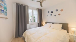 Une chambre à coucher comprenant un lit, un ventilateur de plafond, une fenêtre avec des rideaux et des miroirs fixés au mur.