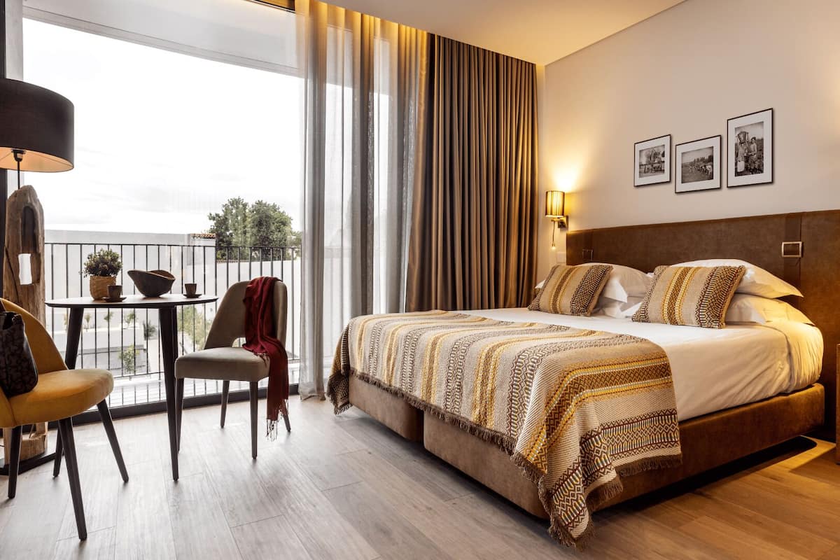 Ein Hotelzimmer mit einem großen Bett, einem Balkon mit Tisch und Stühlen und Blick ins Freie.