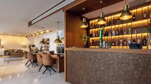 Un espace bar moderne avec un comptoir en bois, de nombreuses suspensions décoratives et une variété de bouteilles d’alcool.