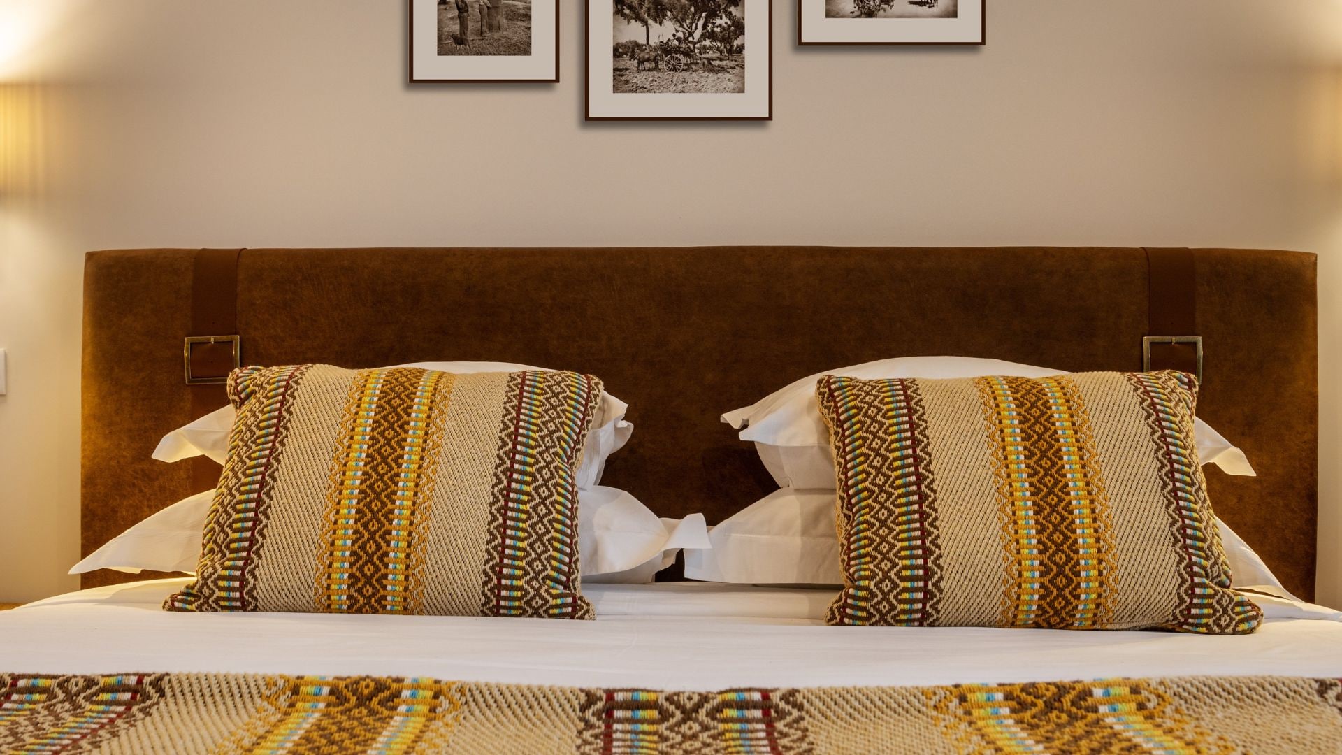 Cama com duas almofadas estampadas e um cobre-leito combinando, apoiada em uma cabeceira marrom.
