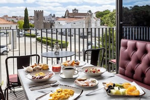 Une table sur le balcon avec des éléments pour le petit-déjeuner, une vue sur un bâtiment historique et un canapé en cuir rouge.