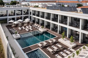 A rooftop pool area with multiple lounge chairs and umbrellas, surrounded by a modern building with balconies. - Évora O Cante Hotel (Évora)