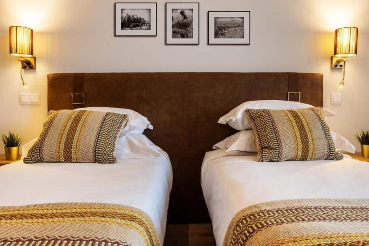Ein Hotelzimmer mit zwei Betten, jeweils mit gemusterten Bettbezügen und Kissen, sowie Wandleuchten.