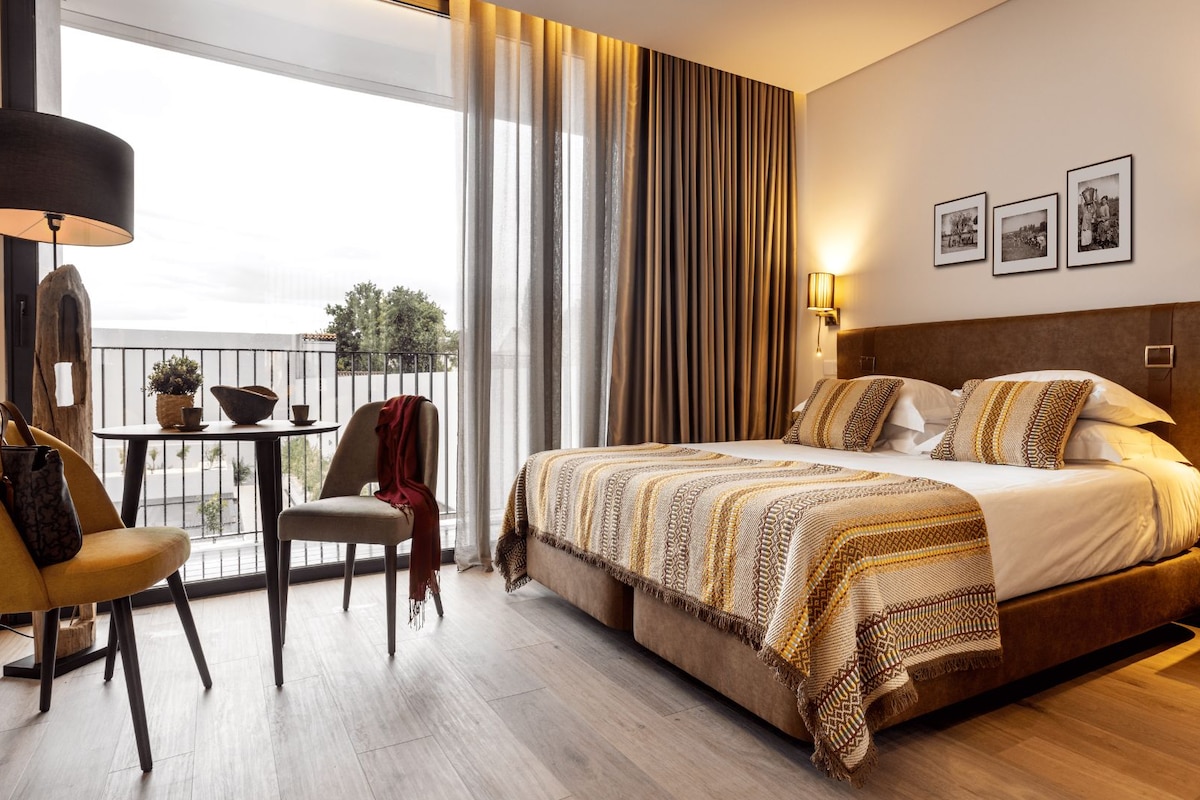 Une chambre d’hôtel avec un grand lit, un balcon doté d’une table et de chaises, et une vue sur l’extérieur.