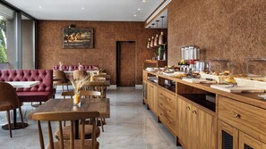 A modern restaurant with a red sofa, wooden tables, and a buffet counter with various food items. - Évora O Cante Hotel (Évora)