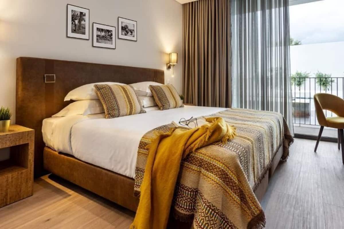Ein modernes Hotelzimmer mit einem großen Bett, einem Schreibtisch, einem Sessel und einem Balkon mit Blick.