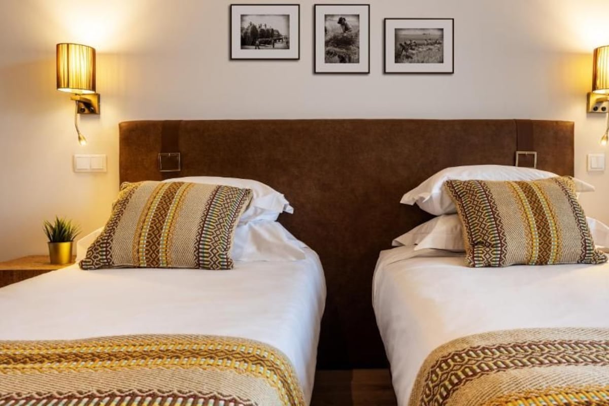 Une chambre d’hôtel avec deux lits, chacun agrémenté de draps et d’oreillers à motifs, et des lampes fixées au mur.