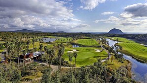 Ein Golfplatz mit Wasserflächen, Palmen und einem Berg im Hintergrund.