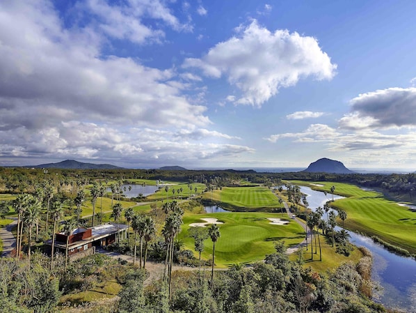 A golf course with water bodies, palm trees, and a mountain in the background. - Mercure Ambassador Jeju (Seogwipo)