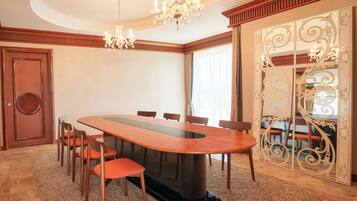 A conference room with a long table, chairs, a chandelier, and a decorative mirror.