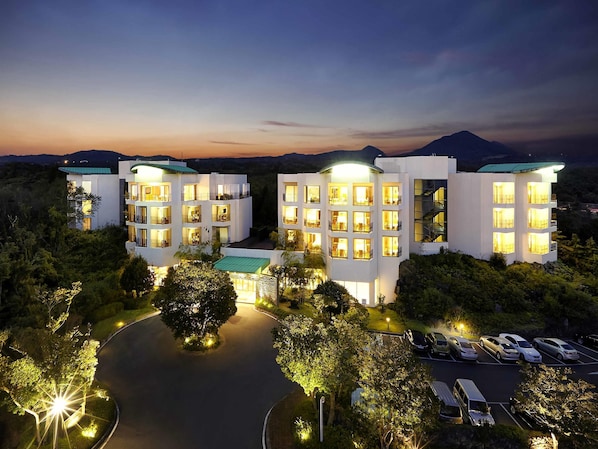 A multi-story hotel with balconies, a parking area, and a view of the surrounding landscape.
