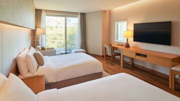 A hotel room with two beds, a desk, a chair, a TV, and a balcony with a view.