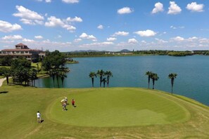 A golf course with a water body, palm trees, and a building in the background. - Gingko Lake Resort Hotel Villa (Nanjing)
