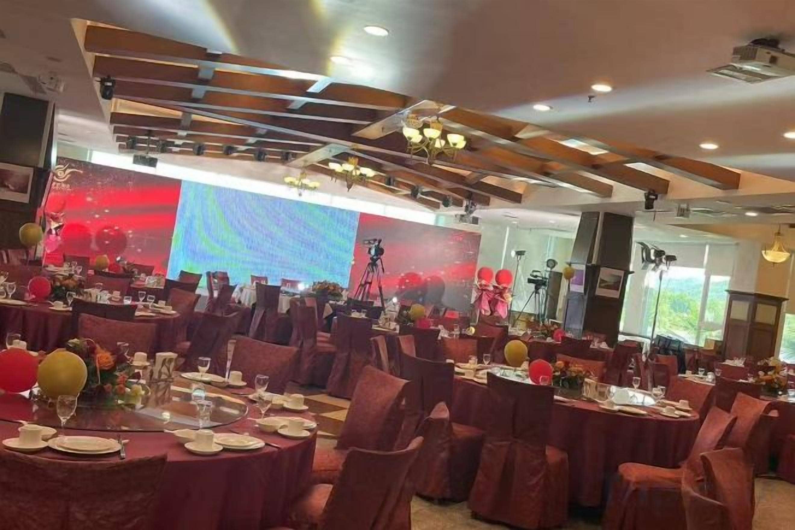 A banquet hall with round tables, chairs, and a large screen in the background.