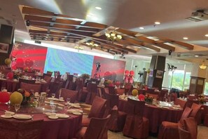 A banquet hall with round tables, chairs, and a large screen in the background. - Gingko Lake Resort Hotel Villa (Nanjing)