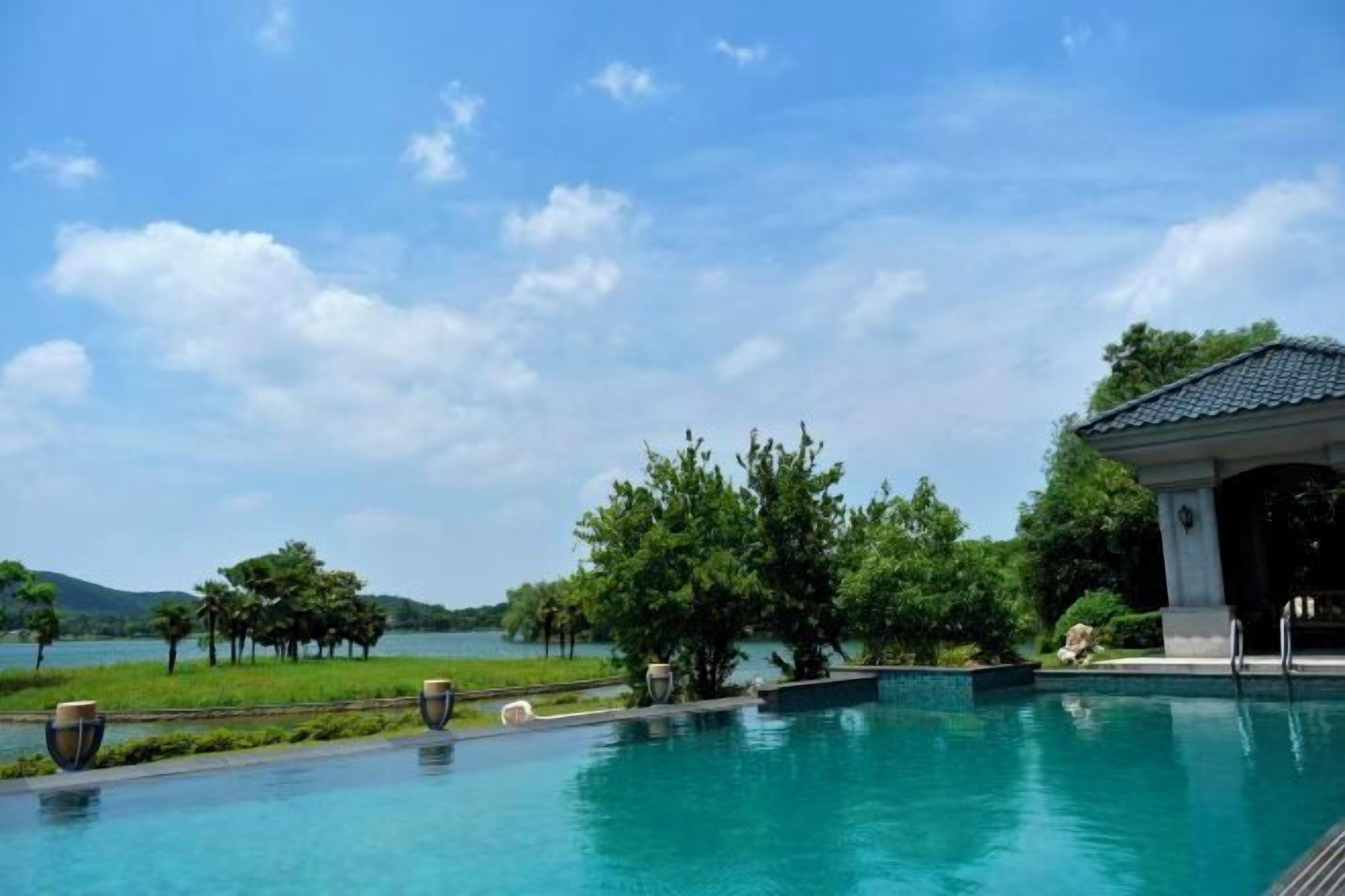 Una piscina con vistas a un lago y árboles, un pabellón y un cielo despejado.