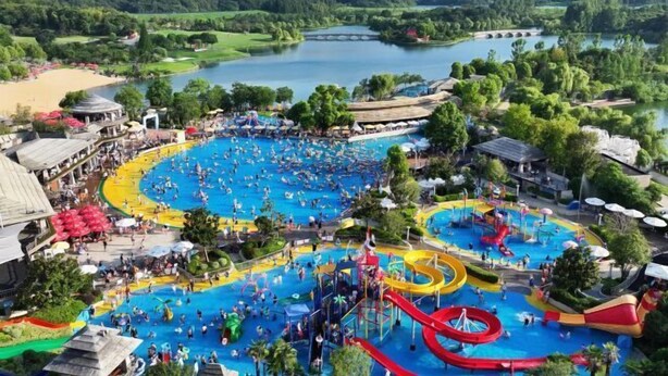 Parque acuático con múltiples piscinas y toboganes, rodeado de exuberante vegetación y un lago.