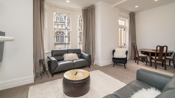 A modern living room with a grey sofa, a round coffee table, and a dining area with wooden chairs and a table. - Inner City Elegance on Stuart Street (Dunedin)