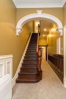 Una escalera con barandilla de madera y detalles blancos, que conduce a una puerta al final.
