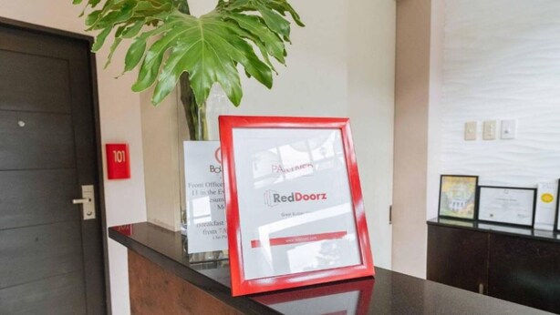 A reception desk with a framed sign, a potted plant, and a door with a red number plate. - Reddoorz @ Garcia Hernandez Bohol (Garcia Hernandez)