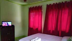 Una habitación de hotel con una cama, un televisor en un aparador y cortinas rojas.