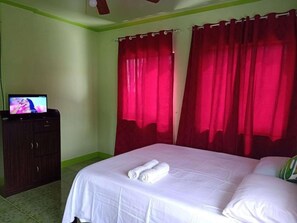 Een hotelkamer met een bed, een televisie op een dressoir en rode gordijnen.