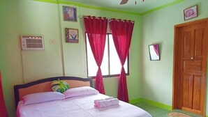 A bedroom with a bed, a window with red curtains, a wooden door, and a wall-mounted air conditioner. - Reddoorz @ Garcia Hernandez Bohol (Garcia Hernandez)