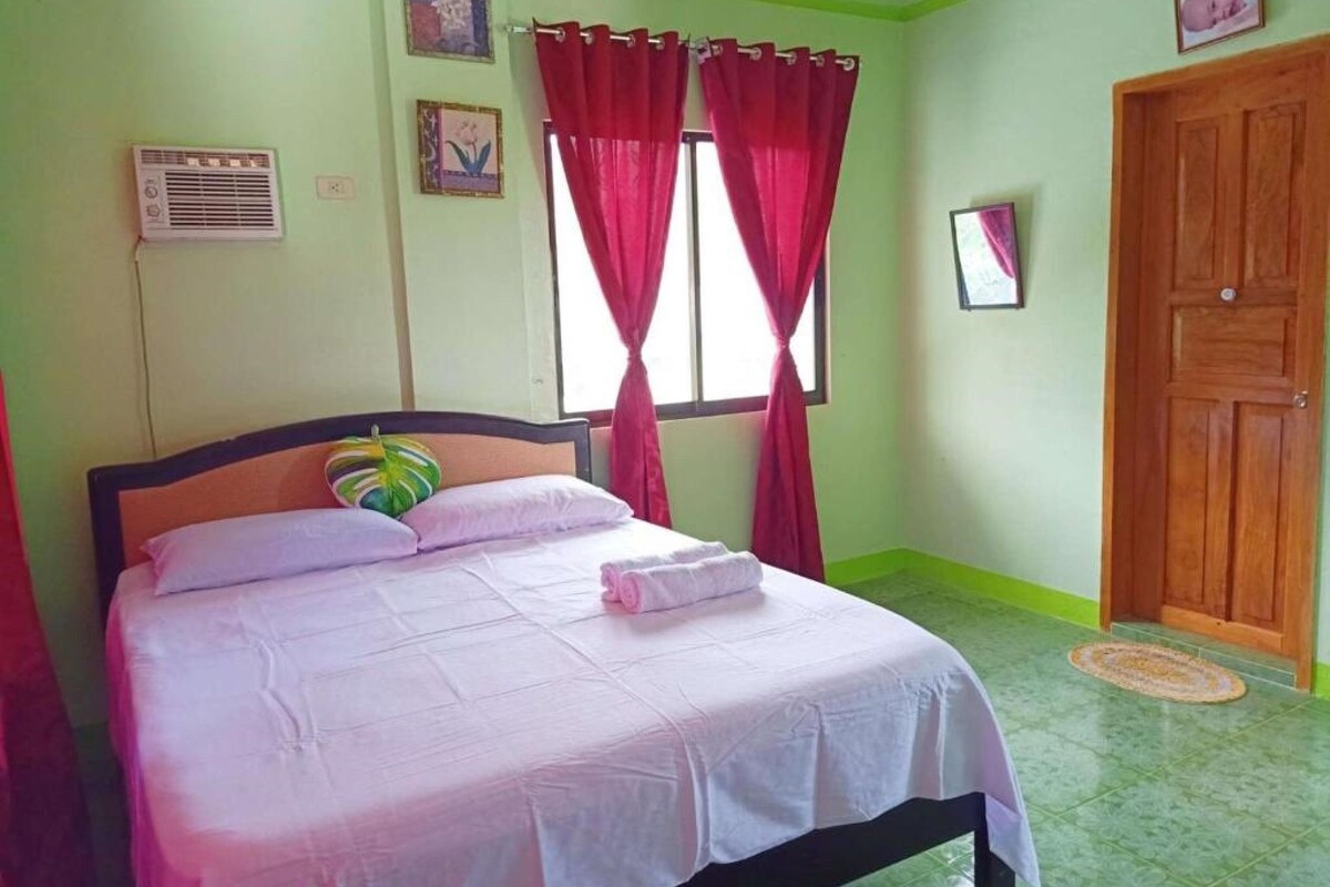 Un dormitorio con cama, ventana con cortinas rojas, puerta de madera y aire acondicionado instalado en la pared.