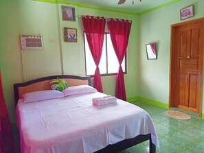 Een slaapkamer met een bed, een raam met rode gordijnen, een houten deur en een airconditioner aan de muur.