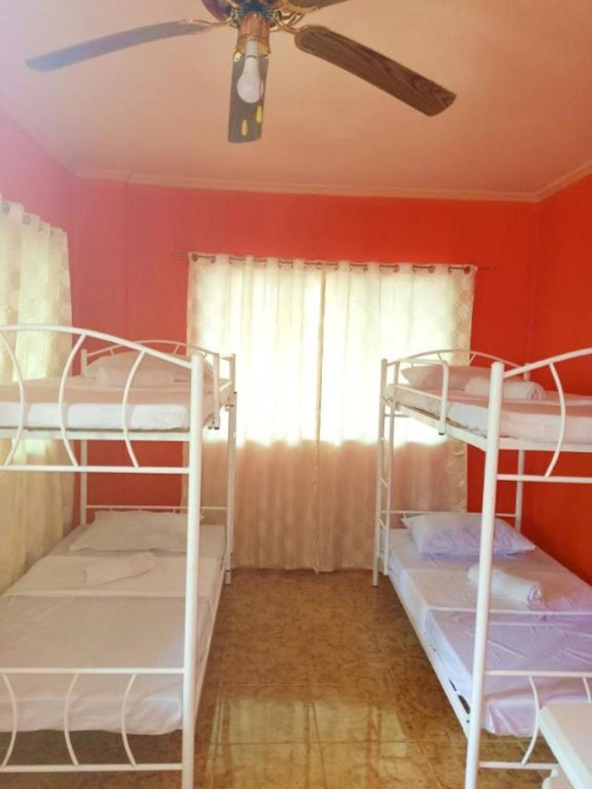 A room with bunk beds, a ceiling fan, and a window with curtains.
