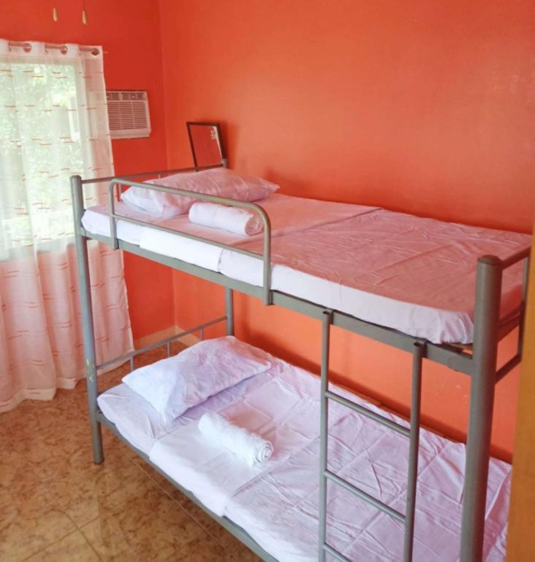 A bunk bed room with orange walls, a window with curtains, and a radiator.