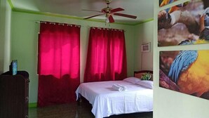 A bedroom with a bed, red curtains, a ceiling fan, and a wall with bird pictures. - Reddoorz @ Garcia Hernandez Bohol (Garcia Hernandez)