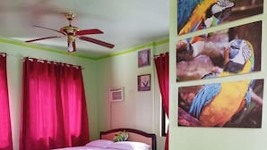A bedroom with a bed, a ceiling fan, red curtains, and three parrot pictures on the wall. - Reddoorz @ Garcia Hernandez Bohol (Garcia Hernandez)