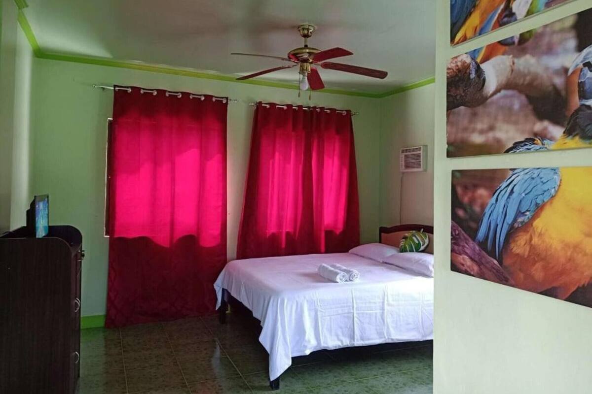 Un dormitorio con cama, cortinas rojas, ventilador de techo y una pared decorada con imágenes de pájaros.