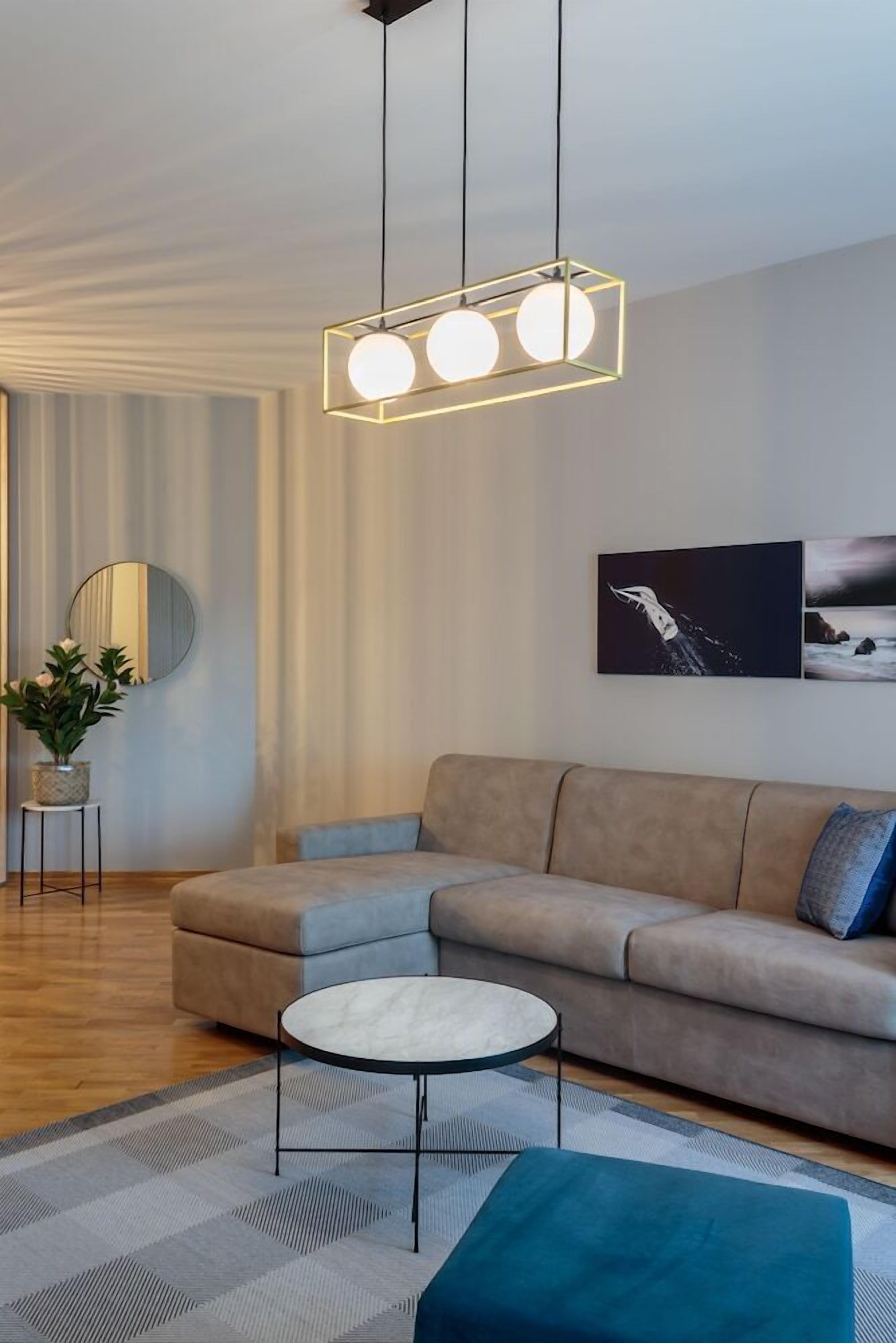 A modern living room with a beige sofa, a round coffee table, and a hanging light fixture with three spherical bulbs.