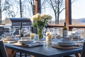 An outdoor dining area with a table set for a meal, surrounded by chairs, and a grill in the background. - Elevation 4118 - an amazing 5 STAR LUXE mountain retreat in Highlands/Cashiers (Highlands)