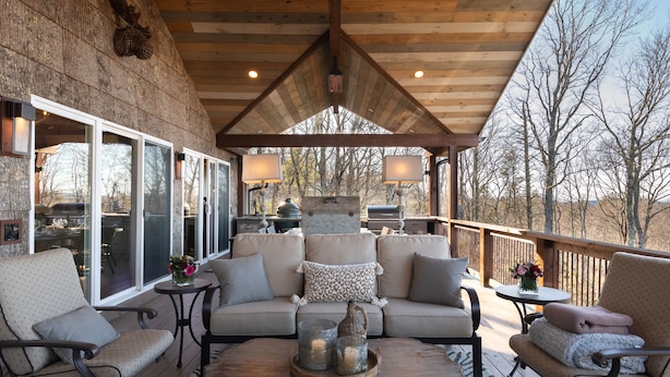 Un espacio al aire libre con techo, que cuenta con una terraza de madera, un conjunto de sofás y una parrilla.