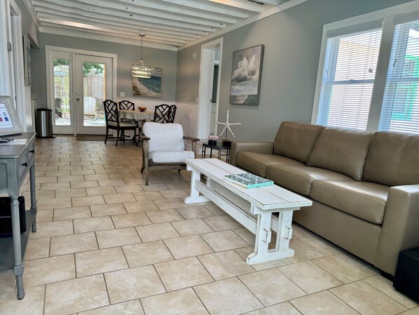 A spacious living room with a beige leather sofa, a white coffee table, and a dining area with a wooden table and chairs. - ⚡2 Blocks from Tybee Pier & Pavilion ⚡ (Tybee Island)