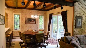 Un comedor con una mesa y sillas de madera, una araña y ventanas grandes con cortinas.