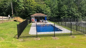 Un patio trasero cercado con piscina, un área de estar cubierta y una terraza de madera.