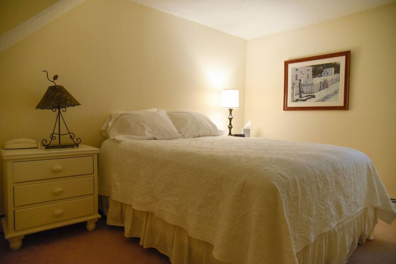 Una camera da letto con un letto, un comodino, una lampada e un quadro appeso al muro.